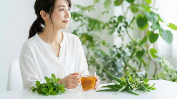 朝の光の中でハーブティーと新鮮な植物が置かれたテーブルと、リラックスした表情の女性